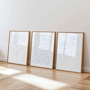 May include: Three framed prints with blue line drawings of flowers. The prints are in wooden frames and are hanging on a white wall.