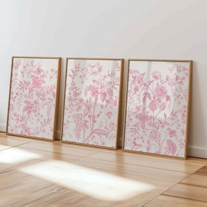 May include: Three framed prints featuring a pink floral design on a white background. The frames are a light wood colour.