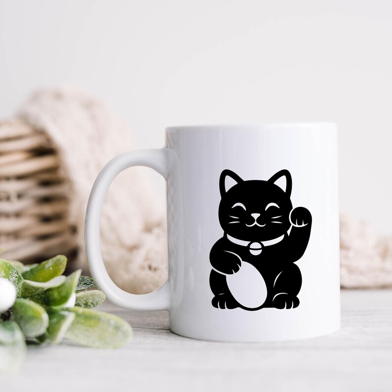May include: White ceramic mug featuring a black illustration of a Maneki-neko cat with a raised paw. The cat has a white collar with a bell. The mug has a curved handle and is set against a neutral background.
