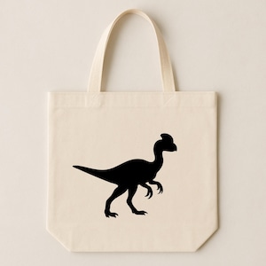 May include: A cream-coloured tote bag with a black silhouette of a dinosaur. The dinosaur is shown in profile, with a long tail, clawed feet, and a distinctive head crest. The bag has two beige handles.