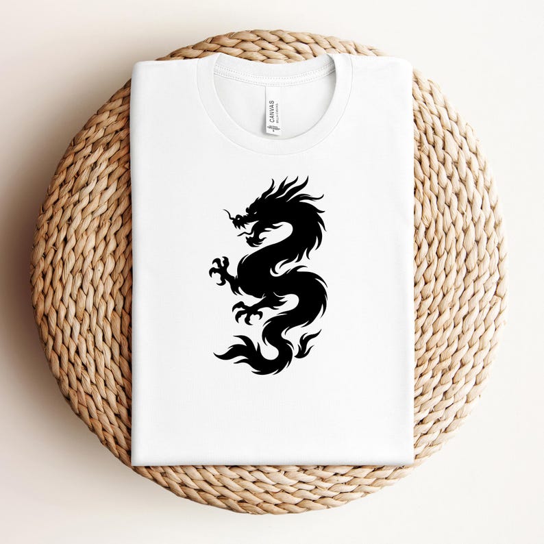 May include: A white t-shirt featuring a black dragon design. The dragon is a stylized silhouette, with intricate details. The shirt is displayed on a round, woven surface.