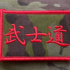 May include: Red embroidered patch with the Chinese characters for "The Way of the Warrior" on a camouflage background.