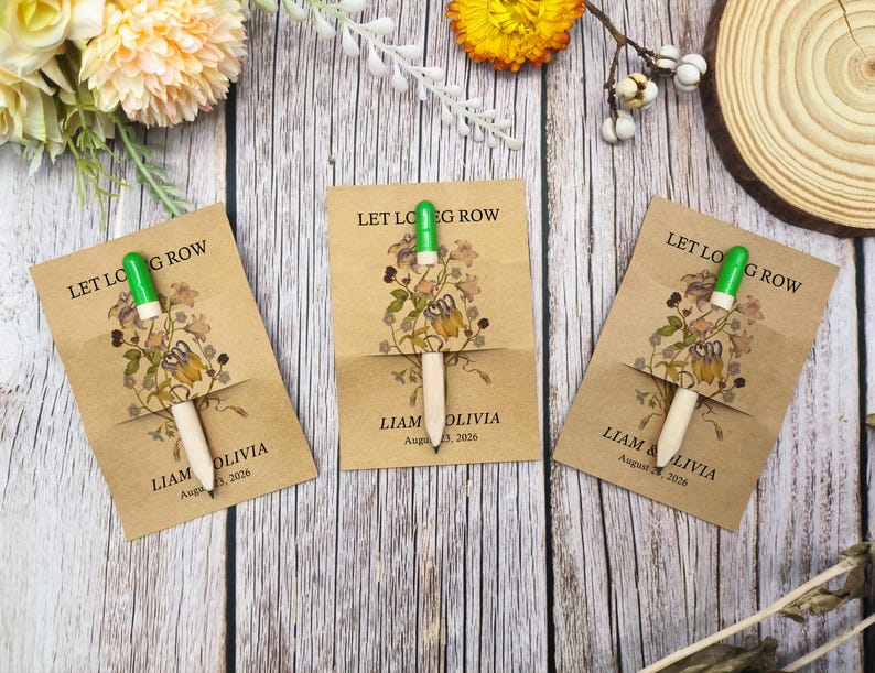 May include: Three seed packet favours with a wooden pencil-like tool and green tip. Each packet is tan with floral illustrations and the text "LET LOVE GROW" and names and a date. The favours are arranged on a wooden surface.