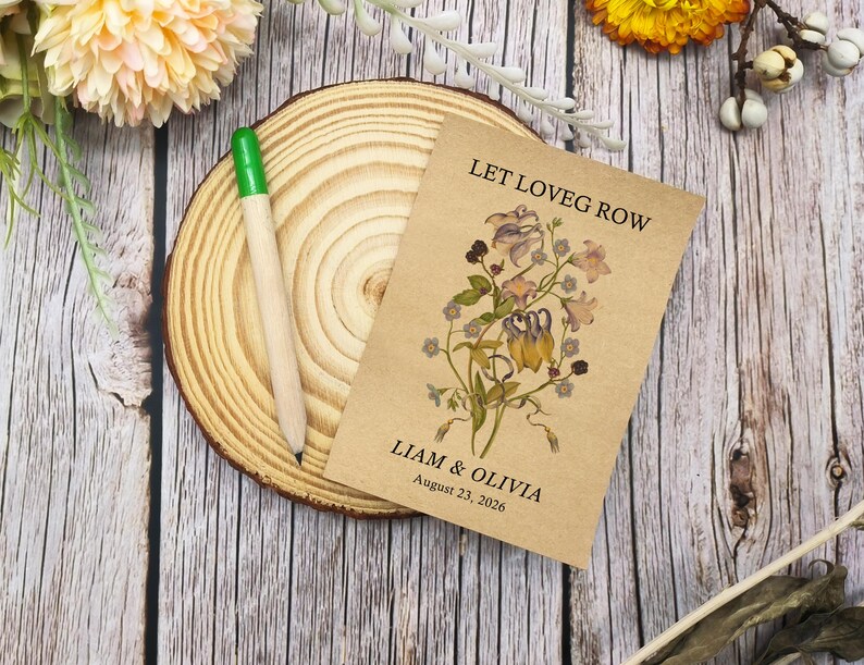 May include: A seed packet with the text "LET LOVEG ROW" and the names "LIAM & OLIVIA" with the date "August 23, 2026" printed on it. The packet features a floral design. A wooden pencil with a green tip rests on a wooden slice.
