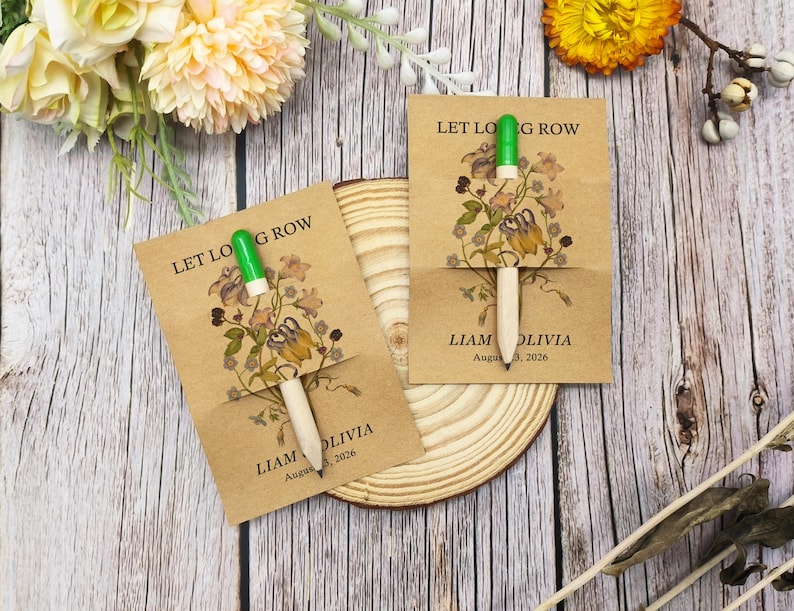 May include: Two seed packet favours with a pen. The kraft paper packets have the text "LET LOG ROW" and "LIAM OLIVIA August 3, 2026" printed on them. The packets feature a floral design and a pen with a green top.
