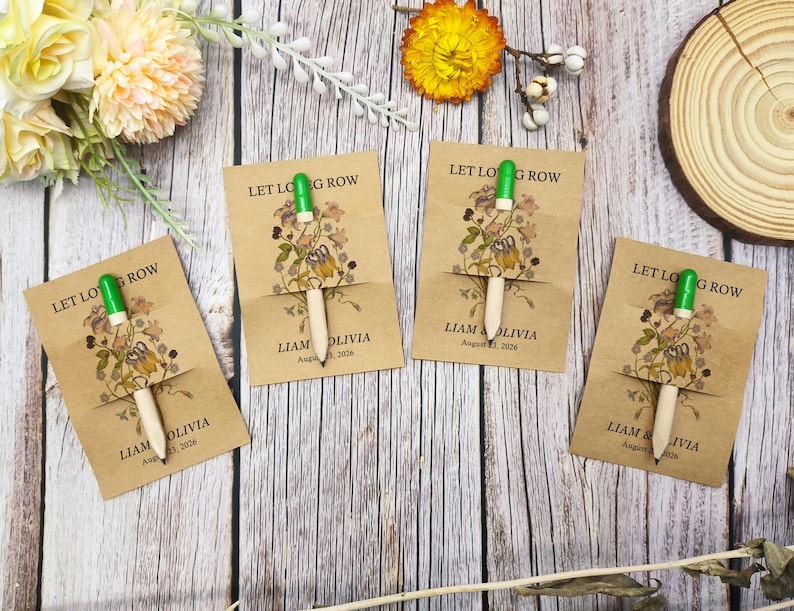 May include: Four kraft paper cards with pencils, featuring floral illustrations and the text "LET LONG ROW". Each card has the names "LIAM & OLIVIA" and the date "August 23, 2026". The pencils have green tops.