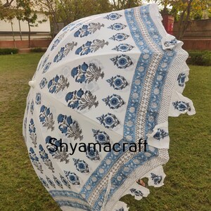 Puede incluir: Una sombrilla blanca y azul con estampado y borde de flecos. La sombrilla est&aacute; hecha de algod&oacute;n y tiene un dise&ntilde;o tradicional indio. El texto "Shyamacraft" est&aacute; impreso en la sombrilla.