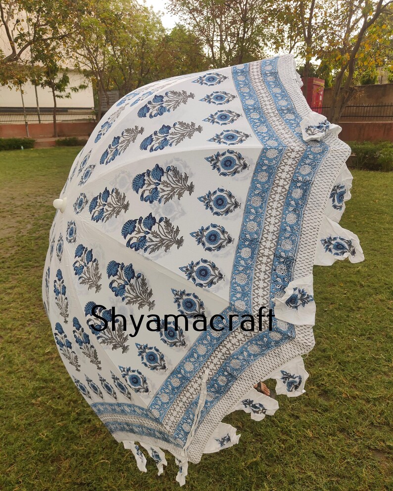 Puede incluir: Una sombrilla blanca y azul con estampado y borde de flecos. La sombrilla est&aacute; hecha de algod&oacute;n y tiene un dise&ntilde;o tradicional indio. El texto "Shyamacraft" est&aacute; impreso en la sombrilla.