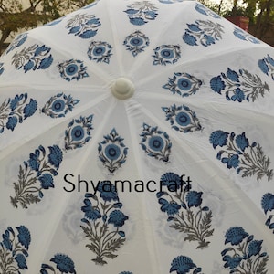 Puede incluir: Paraguas de algod&oacute;n blanco con estampado floral azul. El paraguas tiene un mango blanco y est&aacute; decorado con un patr&oacute;n repetitivo de flores y hojas azules. El texto "Shyamacraft" est&aacute; impreso en el centro del paraguas.