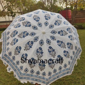 Puede incluir: Paraguas de algod&oacute;n blanco con estampado floral azul y borde de flecos blanco. El paraguas est&aacute; abierto y la parte superior es visible. El texto "Shyamacraft" est&aacute; impreso en el paraguas.