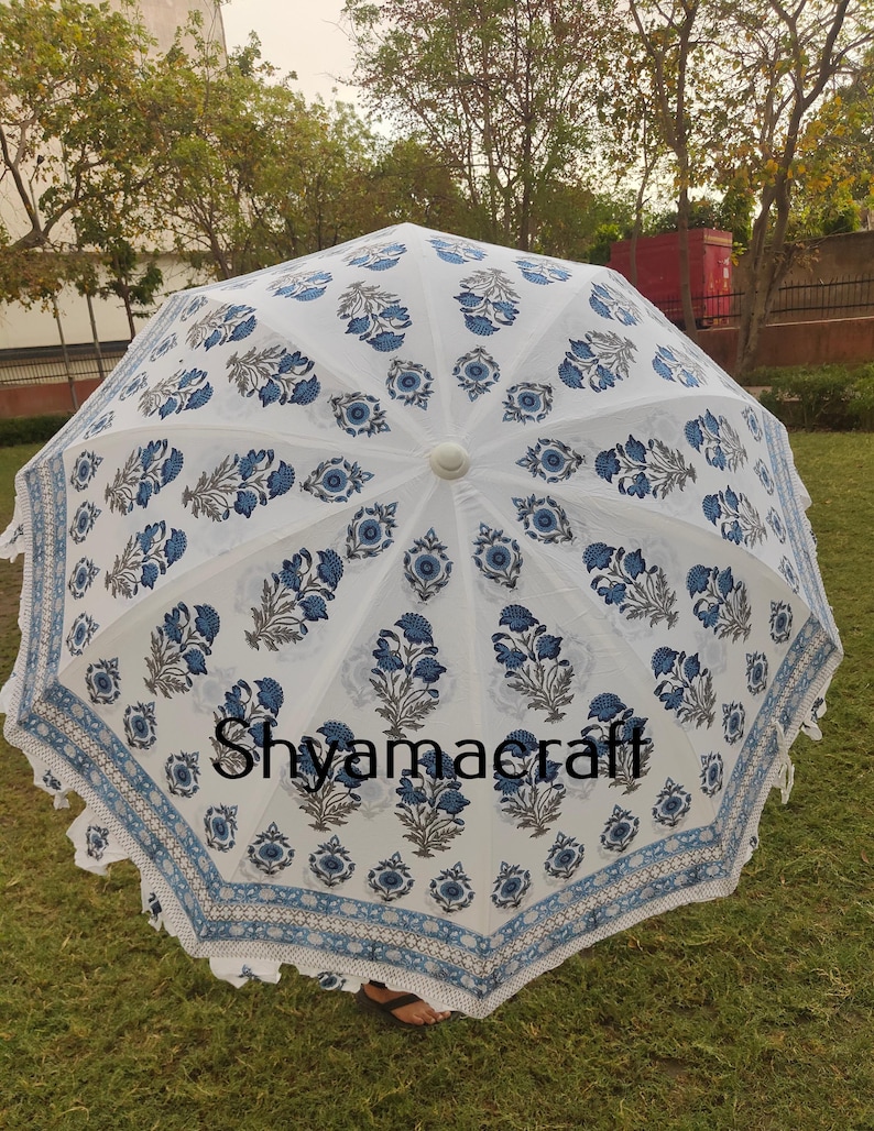 Puede incluir: Paraguas de algod&oacute;n blanco con estampado floral azul y borde de flecos blanco. El paraguas est&aacute; abierto y la parte superior es visible. El texto "Shyamacraft" est&aacute; impreso en el paraguas.