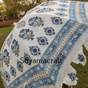Puede incluir: Paraguas de algod&oacute;n blanco con estampado floral azul y gris. El paraguas tiene un borde de flecos y el texto "Shyamacraft" est&aacute; impreso en la tela.