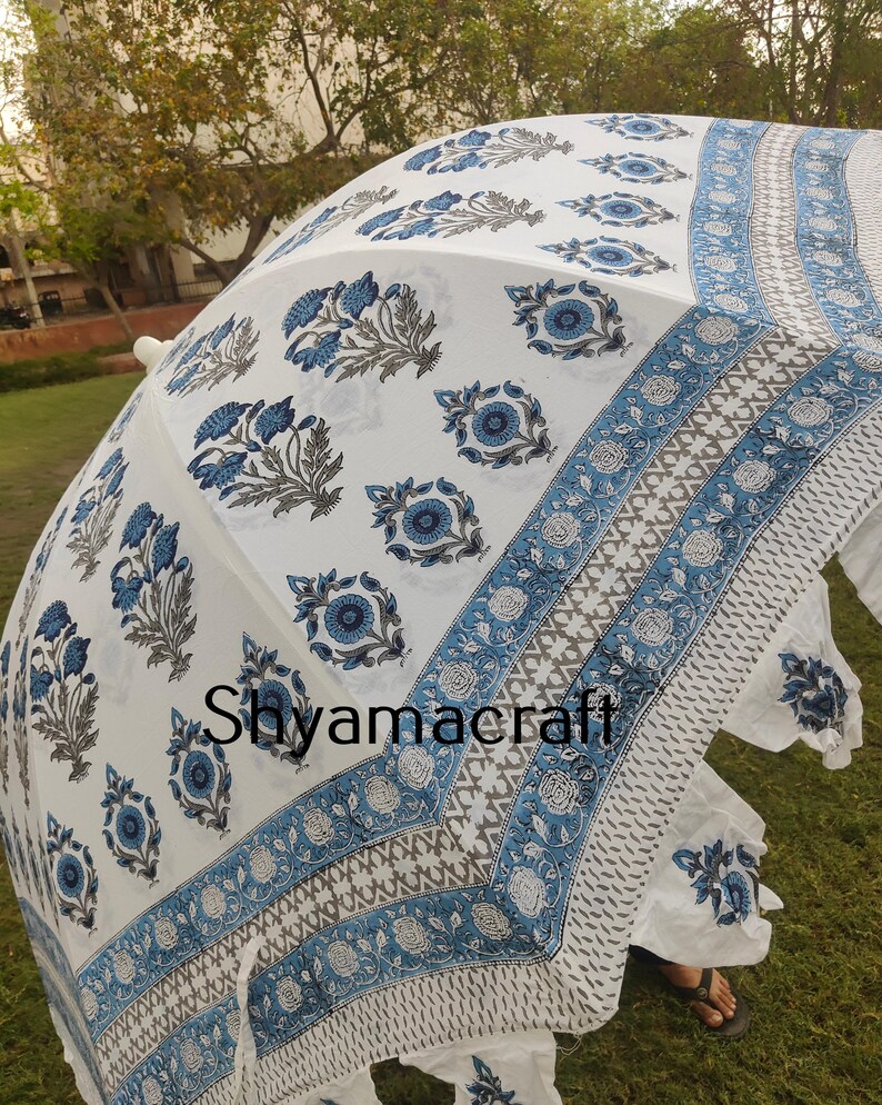 Puede incluir: Paraguas de algod&oacute;n blanco con estampado floral azul y gris. El paraguas tiene un borde de flecos y el texto "Shyamacraft" est&aacute; impreso en la tela.