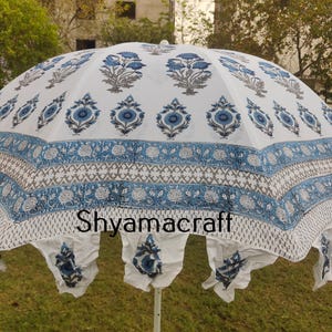 Puede incluir: Paraguas de algod&oacute;n blanco con estampado floral azul y gris. El paraguas tiene un fleco blanco alrededor del borde y las palabras "Shyamacraft" impresas en la tela.