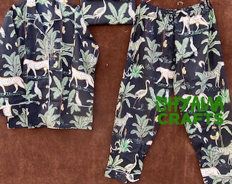 May include: Black pajama set with a white trim. The fabric features a jungle print with zebras, leopards, birds, and palm trees. The set includes a long-sleeved top with a collar and a pair of pants.