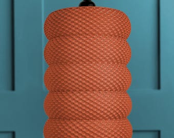 May include: A cylindrical pendant light fitting featuring a textured, woven terracotta-coloured shade with five distinct horizontal ribbed sections. The lamp is suspended from a black cord and a black circular ceiling mount at the top centre.