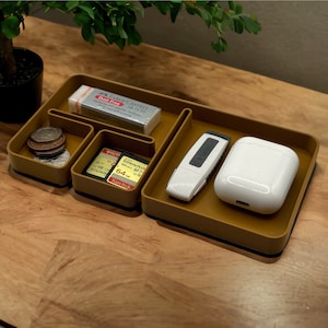 May include: A brown leather-like tray with compartments for organizing small items. The tray has a compartment for coins, a compartment for memory cards, a compartment for a USB drive, and a compartment for a small white case. The tray also has a compartment for a small eraser with the text "Faber-Castell Dust-Free 18/170" printed on it.