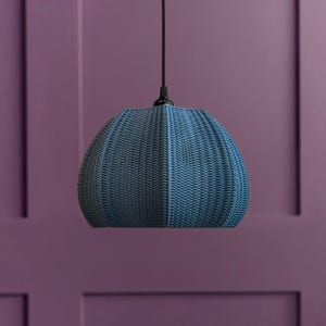 May include: A blue woven pendant light with a rounded, textured shade. The light hangs from a black cord against a purple wall. The shade has a unique, basket-like design.
