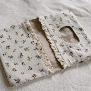 May include: A rectangular fabric wipe dispenser case featuring a cream-colored base with a repeating pattern of small brown and green leaves. The case has a central rectangular opening and decorative ruffled fabric trim along the inner edges.