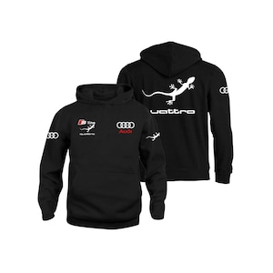 Può includere: Felpa con cappuccio nera con un logo Audi bianco e il testo "S line quattro" sul davanti. La parte posteriore della felpa presenta una lucertola bianca con il testo "quattro" sotto.