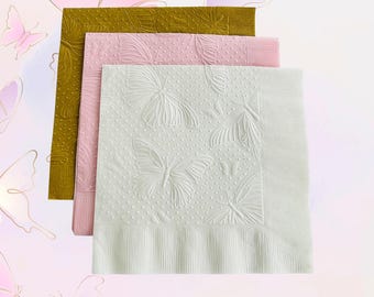 Könnte beinhalten: Drei gestapelte Papierservietten in Olivgrün, Rosa und Weiß. Die weiße Serviette zeigt geprägte Schmetterlinge und ein gepunktetes Muster. Die rosa Serviette hat eine strukturierte Oberfläche, die grüne ein Blättermuster.