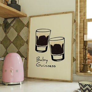 May include: A framed print with a white background and a black and white illustration of two shot glasses filled with a dark liquid. The text "Baby Guinness" is written below the glasses.