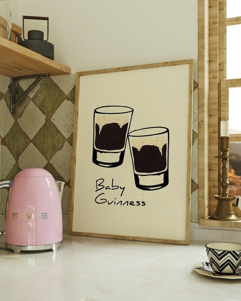 May include: A framed print with a white background and a black and white illustration of two shot glasses filled with a dark liquid. The text "Baby Guinness" is written below the glasses.