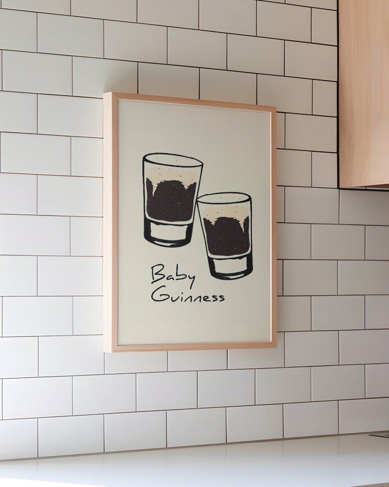 May include: A framed print with a white background and a black and white illustration of two shot glasses filled with a dark liquid. The text "Baby Guinness" is written below the glasses.