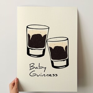 May include: Two small glasses filled with a dark brown liquid topped with a light brown foam. The text "Baby Guinness" is written below the glasses.