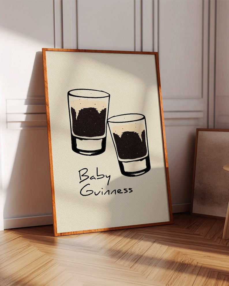 May include: A beige poster with a brown wood frame features a hand-drawn illustration of two small glasses of dark beer with a white head. The text "Baby Guinness" is written below the glasses.