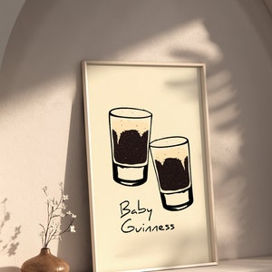 May include: A framed print with a minimalist design featuring two small glasses of dark beer with a light brown head. The text "Baby Guinness" is written below the glasses.