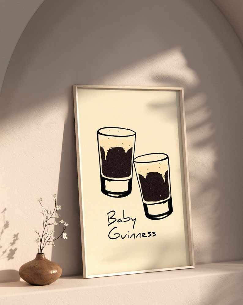 May include: A framed print with a minimalist design featuring two small glasses of dark beer with a light brown head. The text "Baby Guinness" is written below the glasses.