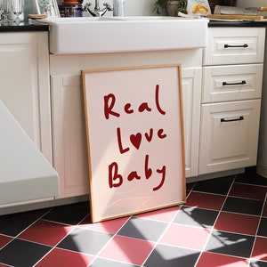 May include: A framed pink poster with the words "Real Love Baby" written in red cursive with a red heart in the word "Love".