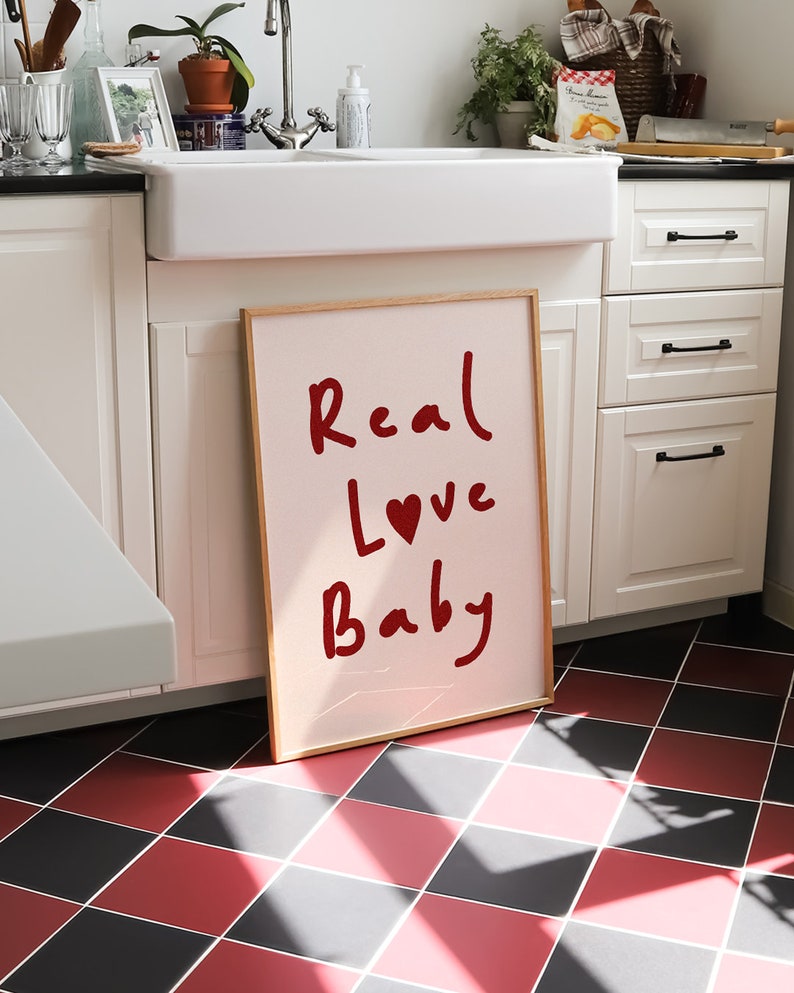 May include: A framed pink poster with the words "Real Love Baby" written in red cursive with a red heart in the word "Love".