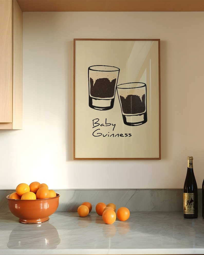 May include: A framed print with a white background and black line drawings of two shot glasses filled with a dark liquid. The text "Baby Guinness" is written below the glasses.