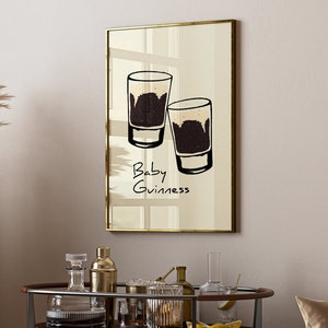 May include: A framed print with a minimalist illustration of two glasses of dark beer with the text "Baby Guinness" underneath.