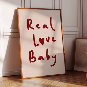 May include: A framed canvas print with the words "Real Love Baby" written in red cursive with a red heart in the word "Love".