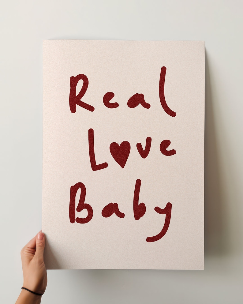 May include: A white poster with the words "Real Love Baby" written in red cursive. A small red heart is included between the words "Love" and "Baby".