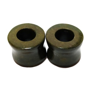 May include: A pair of green wood ear gauges. The gauges are round with a hole in the centre. They are made of a dark green wood with brown and black streaks.