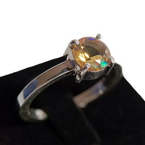 Puede incluir: Un anillo de plata con una piedra preciosa redonda y amarilla engastada en garras.