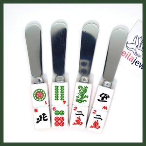 May include: Set of four stainless steel butter knives with white ceramic handles. Each handle features a different Mahjong tile with green and red details. The tiles are numbered 1, 2, 4, and 6, and have Chinese characters on the back.