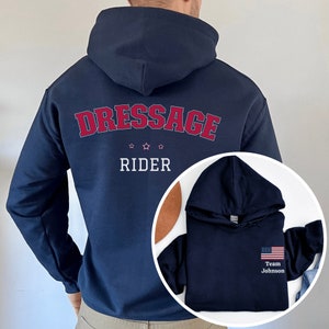 Puede incluir: Dos sudaderas con capucha azul marino. La primera sudadera tiene "Dressage Rider" impreso en la espalda en rojo y blanco. La segunda sudadera tiene una peque&ntilde;a bandera estadounidense y "Team Johnson" impreso en la parte delantera en blanco.