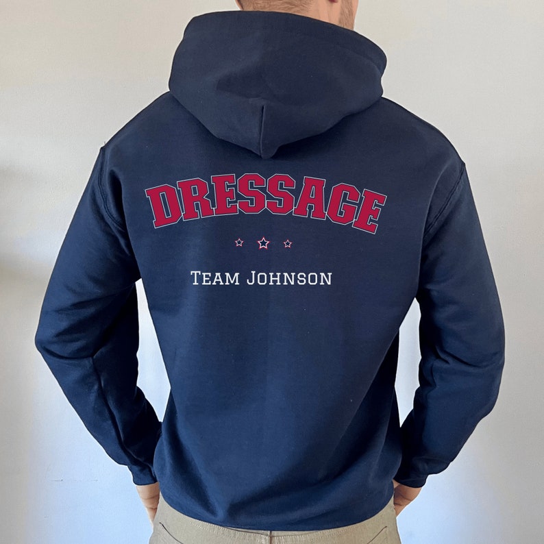 Puede incluir: Sudadera con capucha azul marino con el texto "Dressage" en rojo y "Team Johnson" en blanco. Hay tres estrellas rojas sobre el texto.