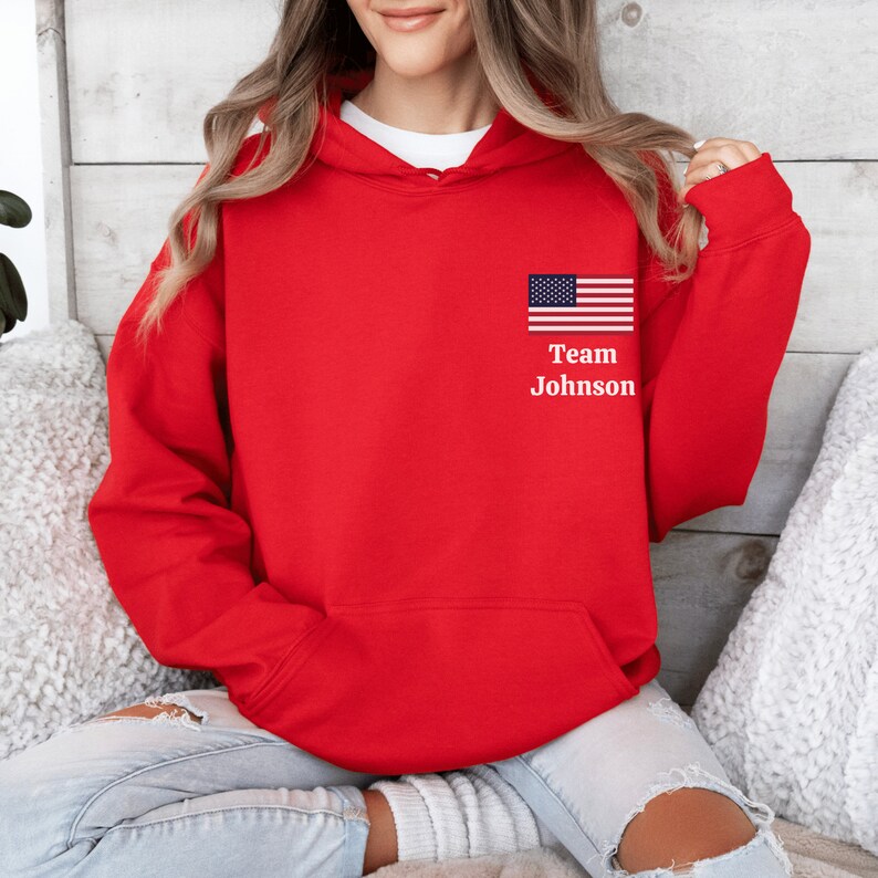 Puede incluir: Sudadera con capucha roja con una peque&ntilde;a bandera estadounidense y el texto "Team Johnson" en la parte delantera.
