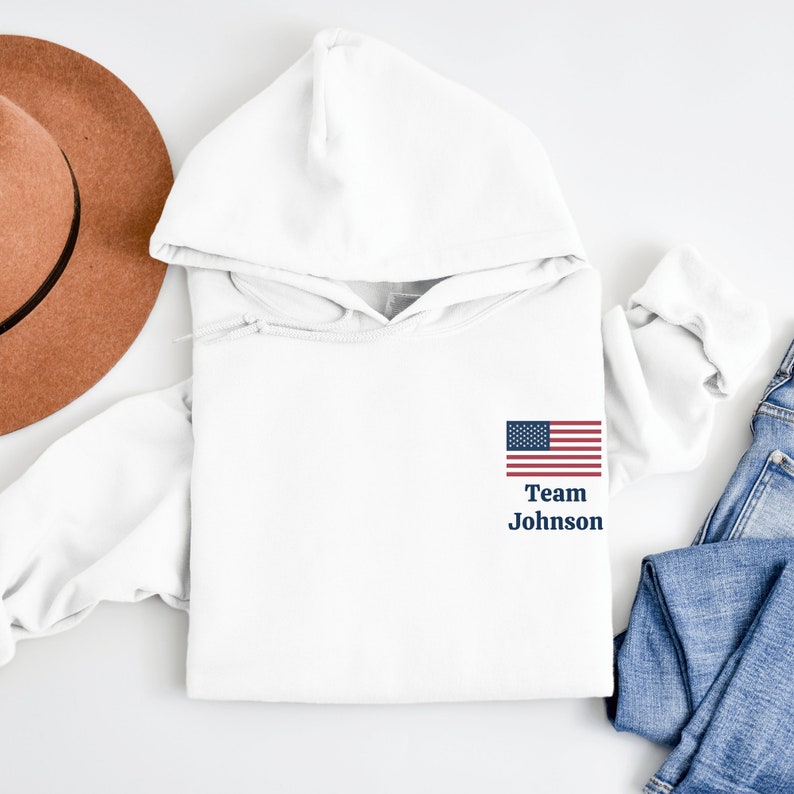 Puede incluir: Sudadera con capucha blanca con una peque&ntilde;a bandera estadounidense y el texto "Team Johnson" en la parte delantera.