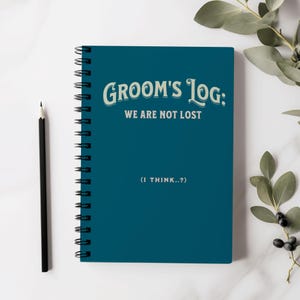 Puede incluir: Una libreta de espiral azul verdosa con el texto "Groom's Log: We Are Not Lost (I Think...?)" en letras blancas y verdes.