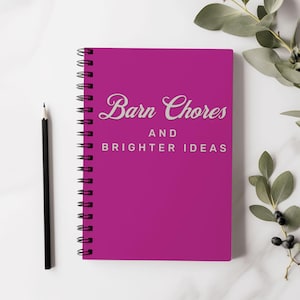 May include: A pink spiral bound notebook with the text "Barn Chores and Brighter Ideas" in white lettering.