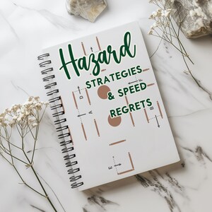 Może przedstawiać: Biały notes w oprawie spiralnej z zielonym i brązowym wzorem. Na okładce notesu widnieje tekst "Hazard Strategies & Speed Regrets".
