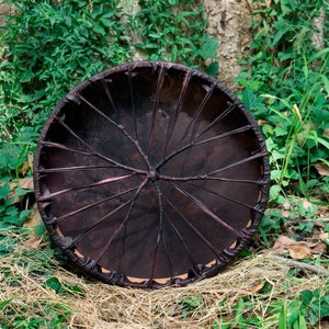 May include: A dark brown leather drum with a circular frame and a pattern of woven leather strips radiating from the center.
