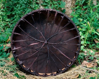 May include: A dark brown leather drum with a circular frame and a pattern of woven leather strips radiating from the center.
